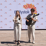 Młoda kobieta śpiewa na scenie. Obok młody mężczyzna akompaniuje na gitarze