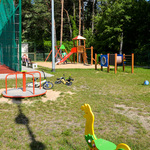 Zdjęcie przedstawia plac zabaw oraz fragment ogrodzonego boisko wielofunkcyjnego.