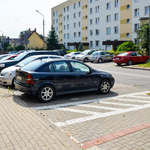 Samochody stoją na parkingu po obu stronach jezdni.