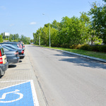 Asfaltowa ulica, wzdłuż której na parkingu po lewej stronie ustawione są samochody.