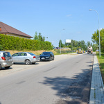 Asfaltowa ulica, wzdłuż której na parkingu po lewej stronie ustawione są samochody.