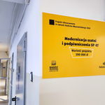 Żółta tablica informująca o modernizacji szatni i podpiwniczenia w Szkole Podstawowej 47 ze środków Budżetu Obywatelskiego.