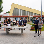 Teren otwarty przed szkołą. Na pierwszym planie prezydent Białegostoku, dyrektorka szkoły i rzeczniczka urzędu miejskiego, obok stół do pingponga, na którym stoi tort i statuetki w kształcie serca. W tle uczniowie i nauczyciele.