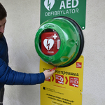 Mężczyzna dotyka dłonią defibrylator AED zamontowany na ścianie.