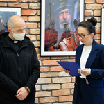 Autor fotografii oraz dyrektorka Centrum Aktywności Społecznej stoją przy ścianie, na której wisi wystawa.