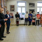 Uczestnicy wernisażu stoją przy ścianach zwróceni w stronę autora fotografii.