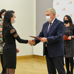 Jasne pomieszczenie. Prezydent Białegostoku podaje dłoń i wręcza teczkę kobiecie w czarnej sukience. W tle dwie kobiety.