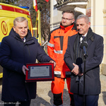 Przed karetką stoją trzy osoby: od lewej prezydent Tadeusz Truskolaski trzymający grawer, lekarz oraz dyrektor Wojewódzkiej Stacji Pogotowia Ratunkowego.