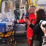 Lekarz-ratownik omawia działanie inkubatora znajdującego się w karetce neonatologicznej. Obok Urszula Boublej - rzecznik prezydenta Miasta Białegostoku trzyma mikrofon.