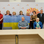 Czlonkowie Białostockiej Rady Seniorów pozują do zdjęcia trzymając dużą ukraińską flagę. 