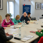 Uczestnicy spotkania siedzą przy stole. Na pierwszym planie Wiceprzewodnicząca Rady Miasta Białystok, w tle członkowie Białostockiej Rady Seniorów. Dwie krótkowłose kobiety robią notatki.