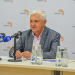 Prezydent miasta siedzi przy stole konferencyjnym. Mówi do mikrofonu. 