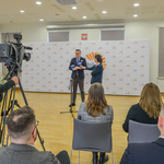 Konferencja prasowa w jasnej, przestronnej sali Centrum Aktywności Społecznej, Zastępca prezydenta Białegostoku mówi do mikrofonu, filmuje go kamera. Uczestnicy spotkania siedzą na krzesłach.