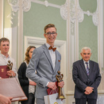 Jakub Klimiuk stoi na scenie podczas odbierania nagrody głównej. W tle prezydent Białegostoku oraz inni wyróżnieni. 