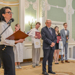Prezydent Białegostoku stoi na scenie wraz z wyróżnionymi wolontariuszami. Prowadząca galę mówi do mikrofonu.
