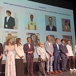 Gala wręczenia nagród. Młodzi wolontariusze i wolontariuszki stoją na scenie. Za nimi, na ekranie wyświetlona jest plansza ze zdjęciami laureatów.